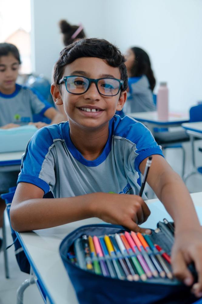 Aluno do Fundamental 1, de óculos, sorrindo na sala de aula